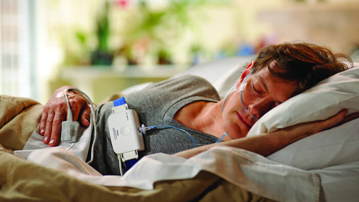 Fotografía de un hombre durmiendo sobre un costado en una cama con un dispositivo para un estudio del sueño de Philips
