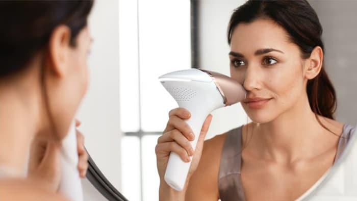 Una mujer frente a un espejo depilándose el bigote con un dispositivo de luz pulsada intensa de Philips.