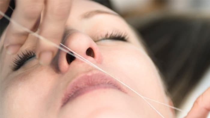 El rostro de una mujer con los ojos cerrados mientras le depilan el bigote con hilo.