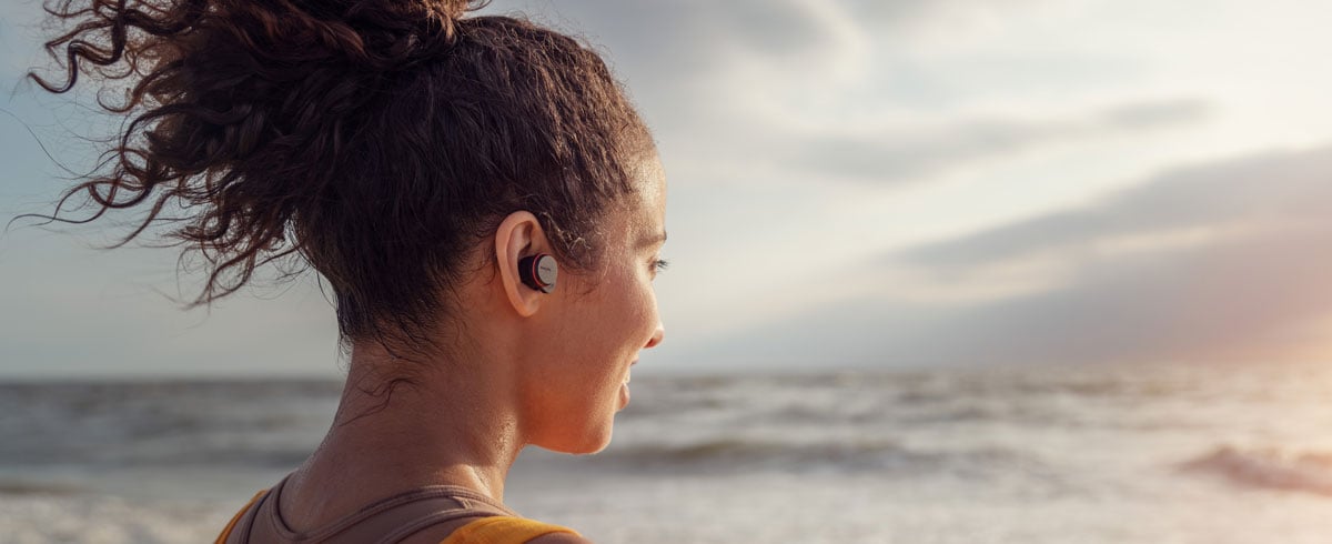 Mujer usando auriculares realmente inalámbricos junto al mar
