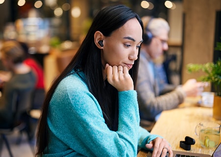 Mujer estudiando en una cafetería usando auriculares inalámbricos con cancelación de ruido Philips T3508