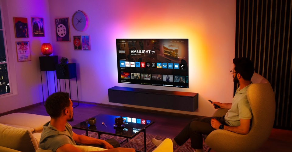 Dos hombres miran un televisor Ambilight montado en la pared en una sala de estar.