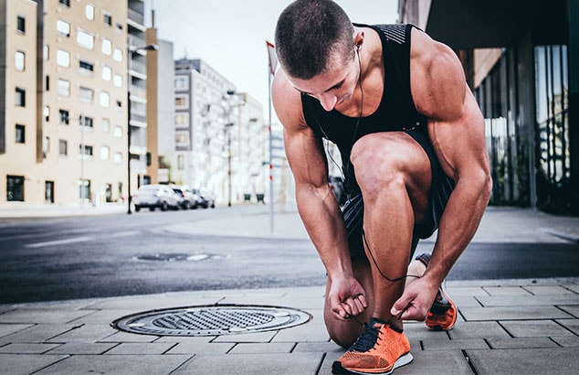 Un deportista musculoso y bien depilado atándose los cordones de las zapatillas en una ciudad