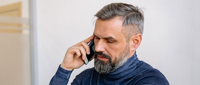 Un hombre con el pelo y una barba gris puntiaguda, bien definida hablando por teléfono mientras mira su reloj