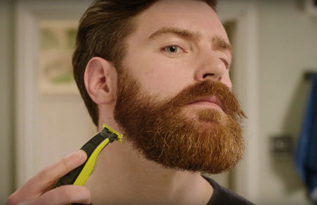 Un hombre afeitándose la barba descuidada hasta dejarla perfecta con una maquinilla y un accesorio específico