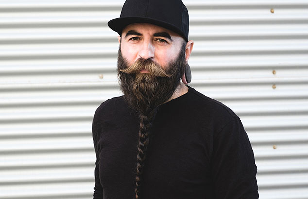 Un hombre con barba vikinga con trenzas, vestido de negro mirando a cámara