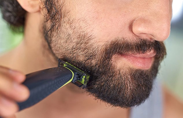 Un hombre afeitándose la barba de tres días, creando un bigote perfilado