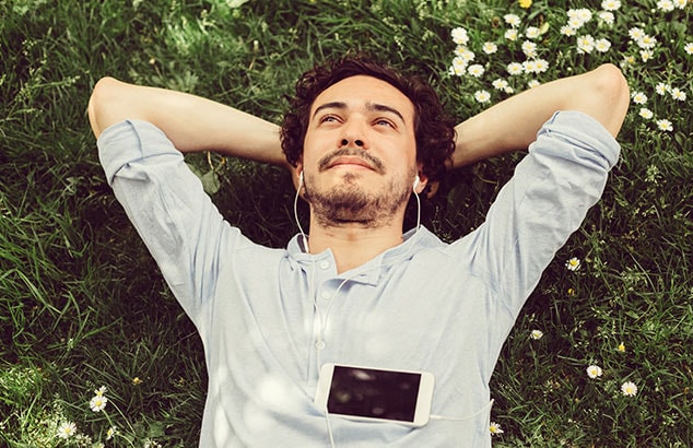 Un hombre sonriente tumbado en el césped escuchando música con auriculares.