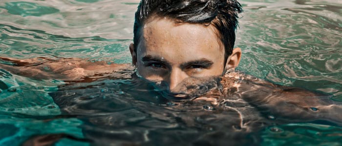 Un hombre nadando en una piscina exterior. Su cuerpo está sumergido en el agua, salvo la mitad superior de su cabeza.