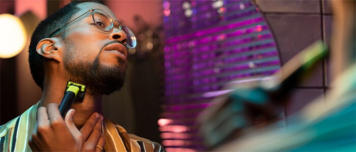 Un chico con gafas afeitándose el contorno de la barba del cuello con Philips OneBlade frente a un espejo