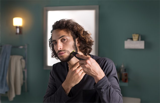 Un hombre perfilándose la barba de la mandíbula con Philips OneBlade en un baño
