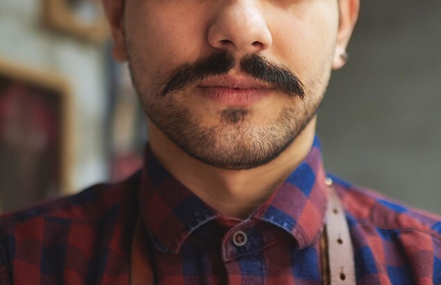 Primer plano de un hombre con un bigote oscuro muy bien recortado que lleva una camisa de cuadros