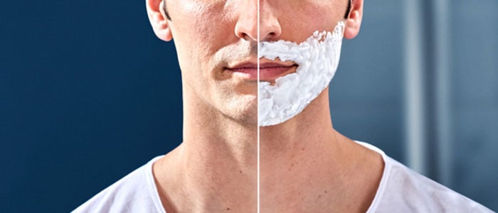 Lado izquierdo de la cara de un hombre bien afeitado y lado derecho con espuma de afeitar en la parte inferior de la cara