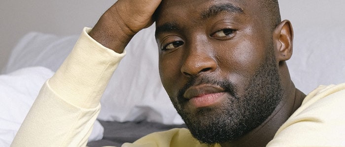 Primer plano de un joven negro con barba corta y sudadera amarilla mirando pensativo a un lado