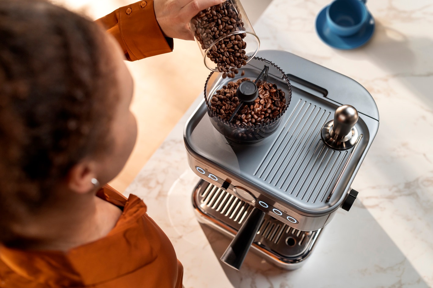 Una joven vierte granos de café en el contenedor de granos de café Barista Brew de Philips