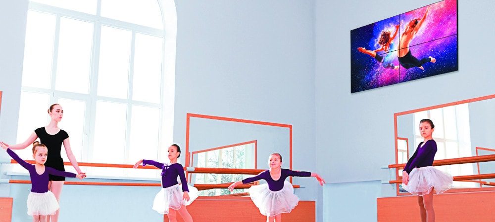 Pantalla de señalización digital en la pared; niños aprendiendo a bailar ballet en una habitación